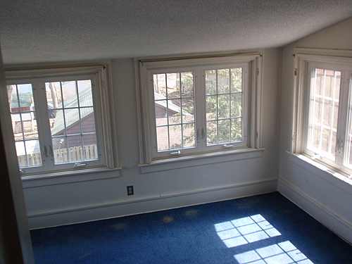 The upstairs, carpeted sunroom at 115 Bulkley. The room has low angles ceilings with at least three sets of casement windows.