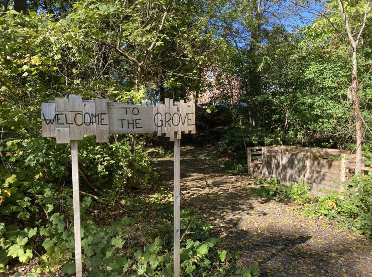 A wooded path, compost bins, and a sign that reads "welcome to the grove"